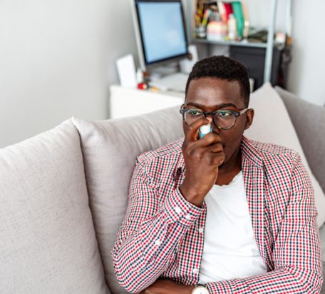 A young male using an inhaler while sitting on his couch at home.